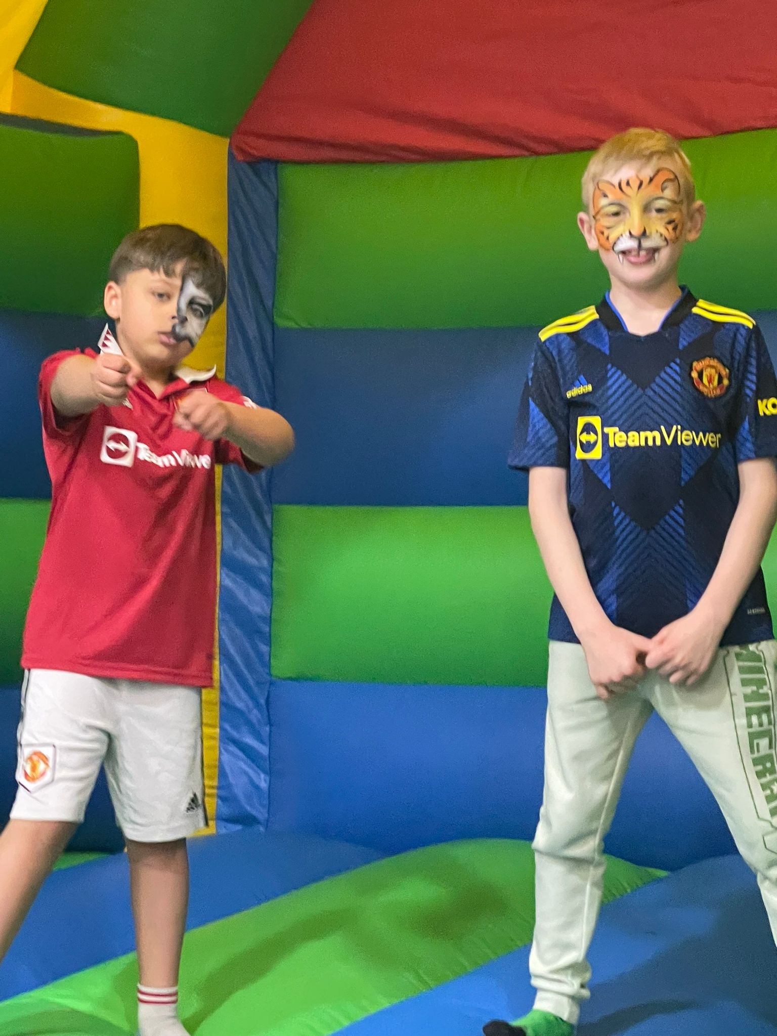 two boys in bouncy castle with their faces painted like a tiger and a skull