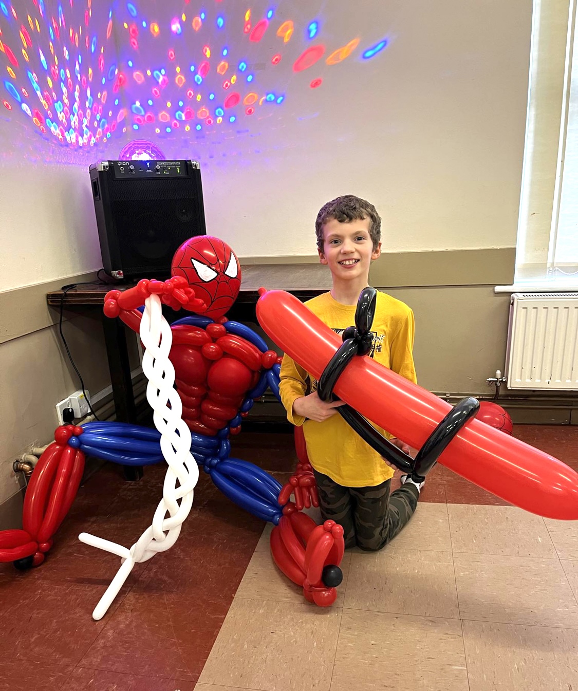 young boy holding giant balloon bazuka gun next to a large spiderman balloon figure at a party in Shrewsbury